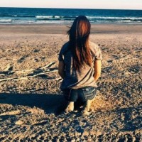 girl sitting on sand looking at ocean