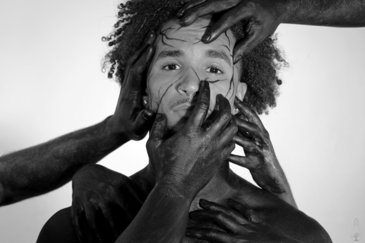 Man staring at the camera. Black hands are all over his face.