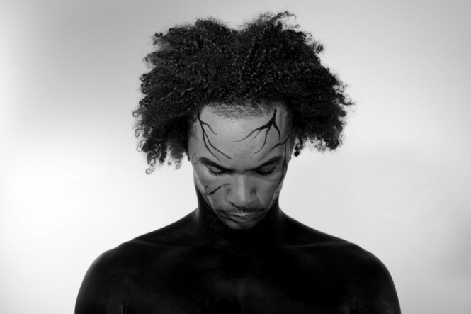 Man with black make up on his body, looking down.