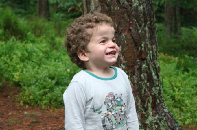 Little boy standing in front of a tree outdoors