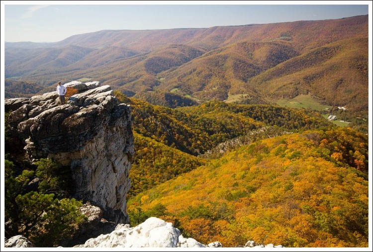 Man on a mountain. The view shows tress and hills. 