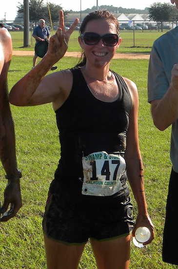 Woman wearing a race bib, smiling and giving the peace sign