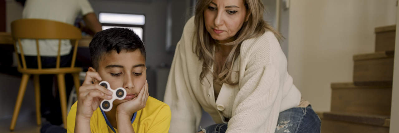 Ideas to Help Parents Calm Their Anxious Child mother & son laying on the floor. The son holds a fidget spinner as they look over a large sheet of paper