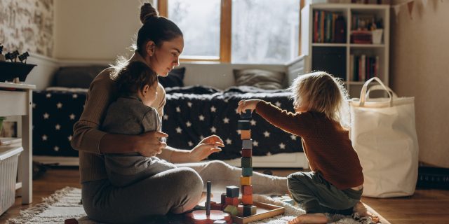 Mother playing with children while sitting on floor at home with wooden toys
