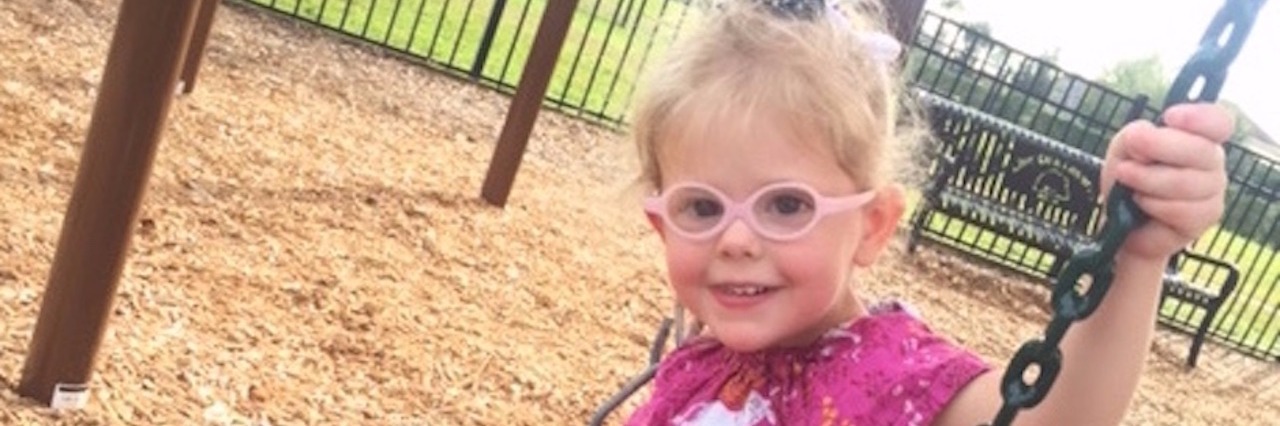 little girl in glasses on a swing