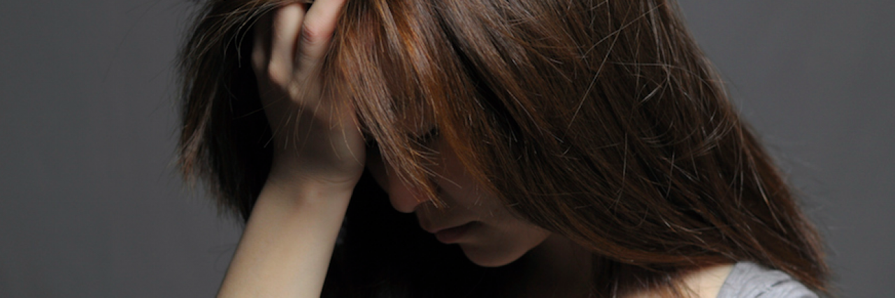 When We Believe Mental Illness Stigma Is True About Ourselves A woman looking down, frustrated, with her hand in her hair