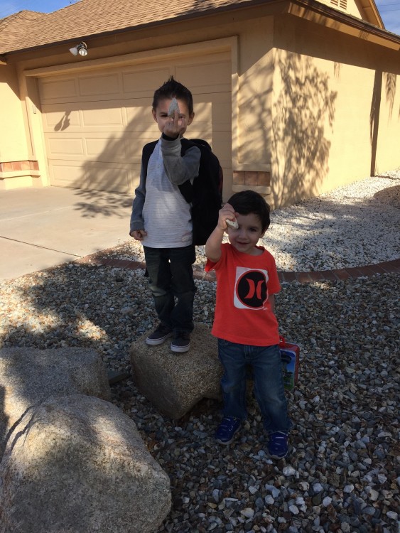 two boys holding up rocks in driveway of house