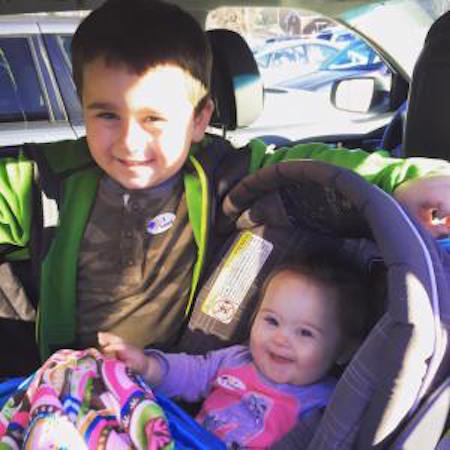 young boy standing next to girl in carseat