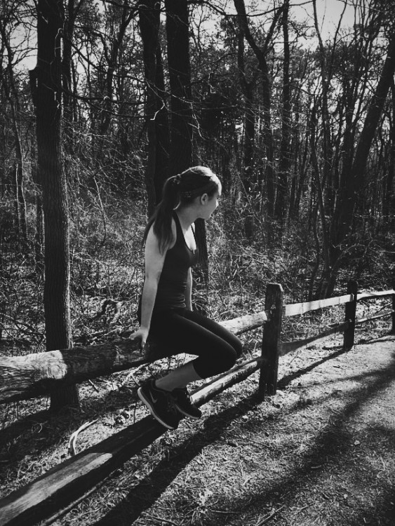 black and white photo of woman sitting on fence in nature