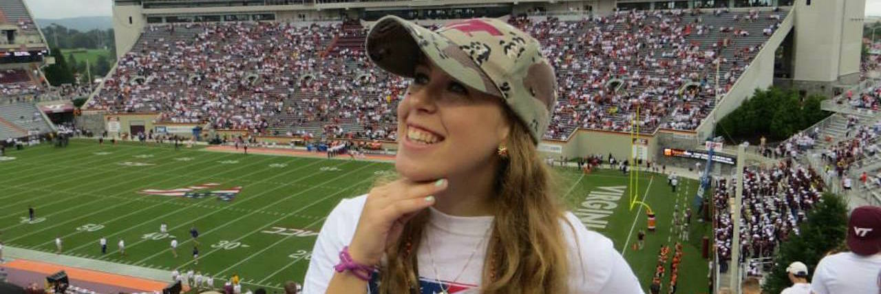When Chronic Illness Can Make You Feel Like a 'Burden' woman smiling with view of football stadium behind