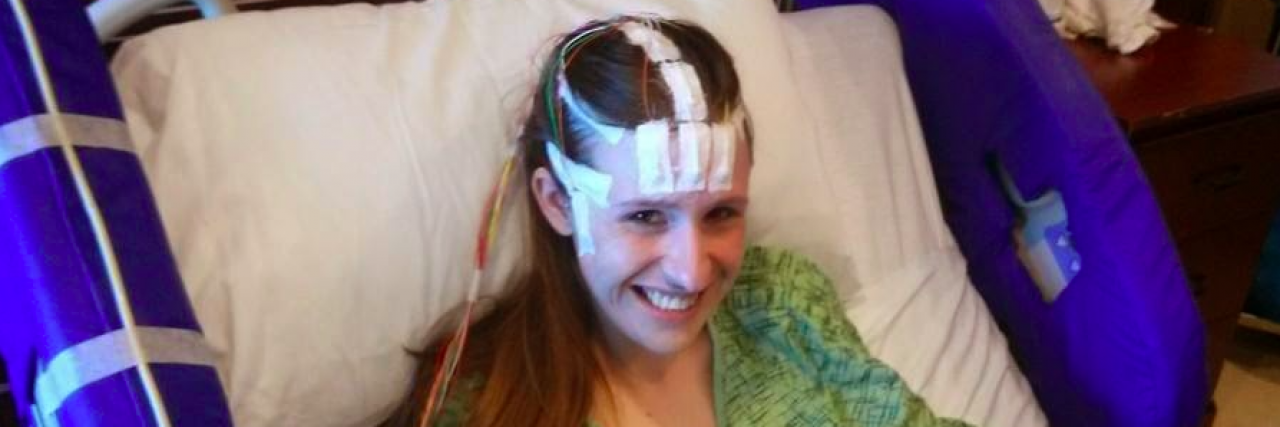 Woman in hospital bed and wires taped to her head smiling and getting an EEG