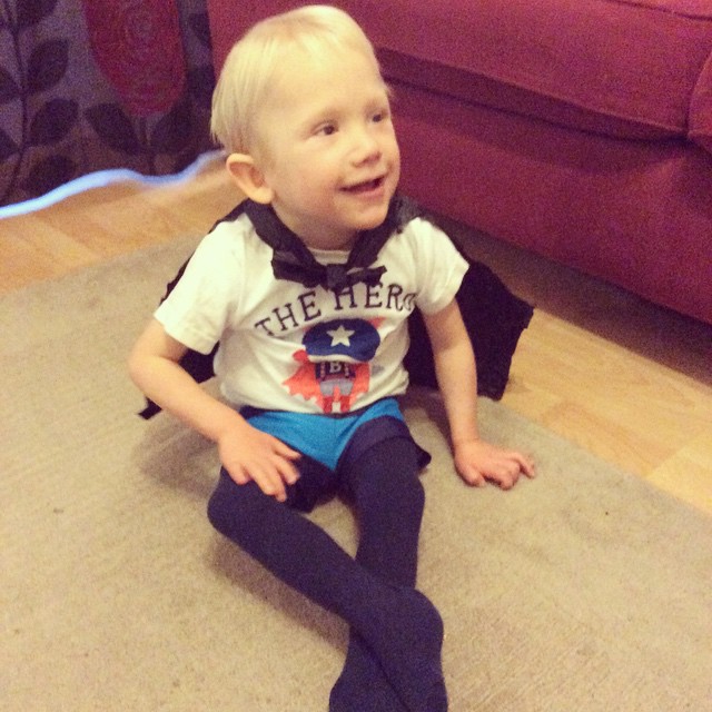 young boy sitting on the floor in superhero cape smiling