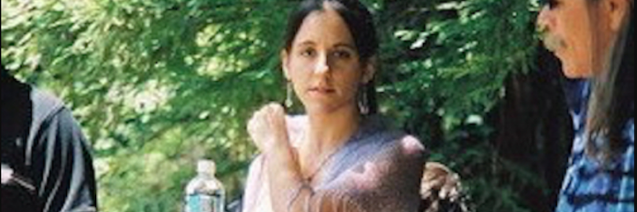 Why I Hide My Chronic Illness The author looking straight ahead and holding a water bottle, wearing a white dress