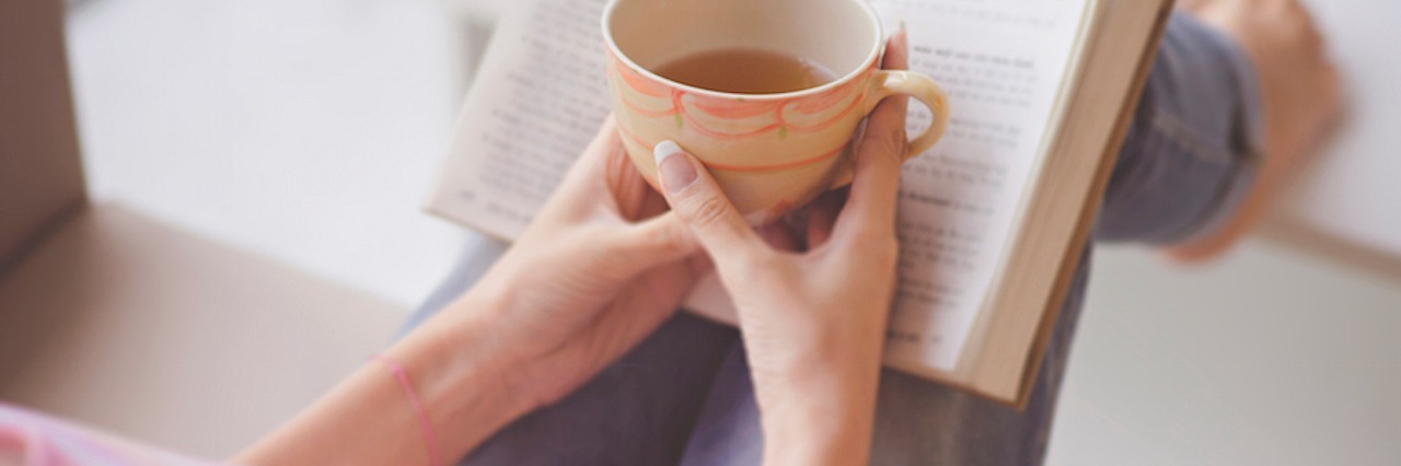 hands holding a teacup in front of an open book