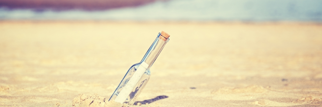 Vintage toned message in a bottle on beach, shallow depth of field.