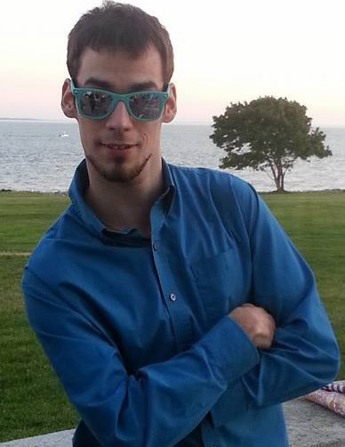 Austin Wykes - young man in a blue shirt with a view of a lake behind him.