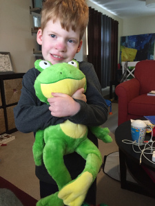 young boy holding stuffed frog to his chest