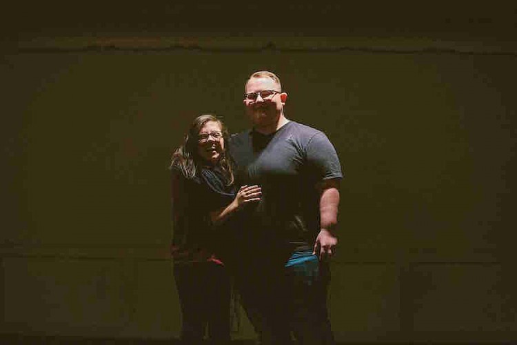 young woman and man standing in front of dark background with arms around each other