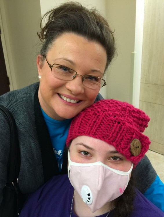 woman smiling with her daughter wearing a red hat and face mask