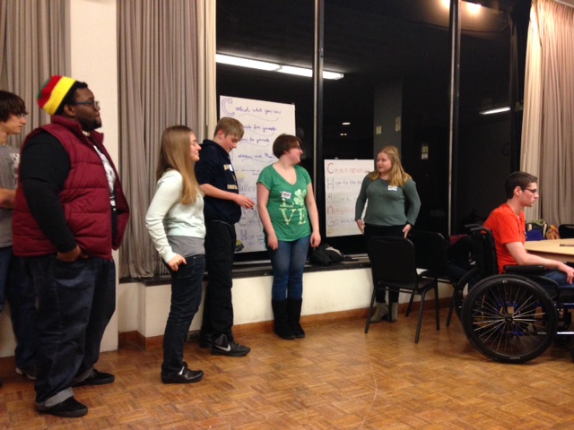 group of teenagers lines up and showing off posters inside room with tall windows