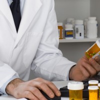 Pharmacist looking at pill bottle and using computer