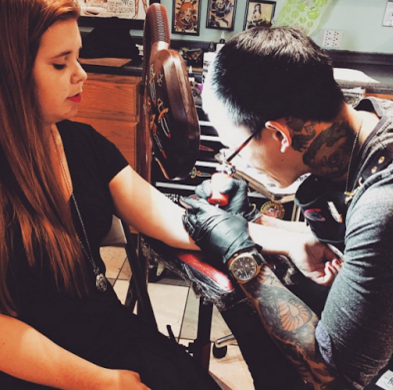 young woman sitting in tattoo parlor getting a tattoo on her arm