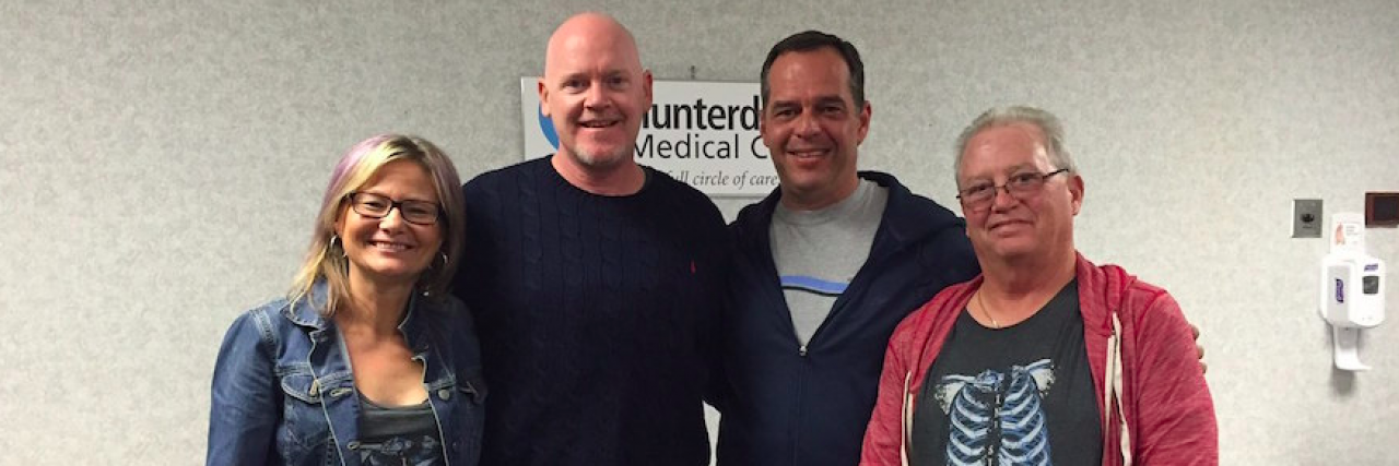Benefits of Chronic Pain, Lupus, and Fibromyalgia Four members of a support group standing in a room in front of table