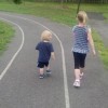 two kids running on a path with grass on each side