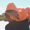 young boy in orange hoodie laughing as he's carried over a man's shoulder