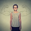 Woman stands in front of a wall with a drawing of two arms flexed, making a muscle behind her