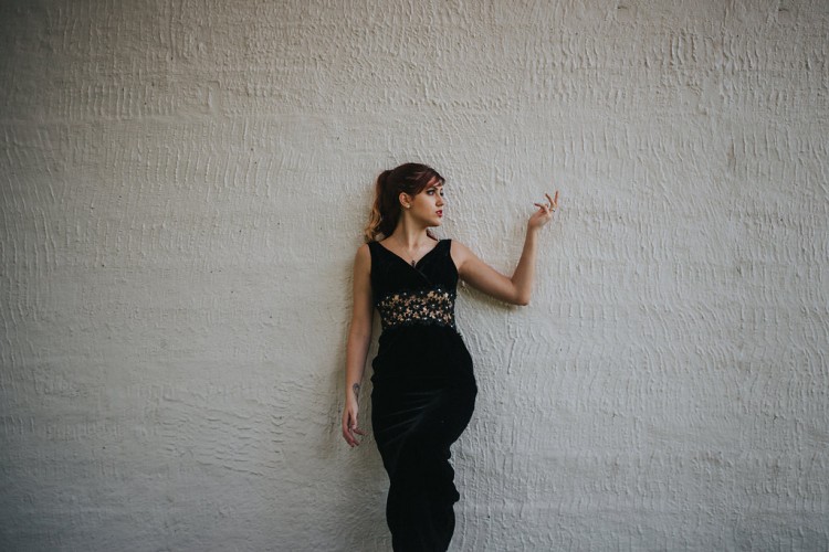 Ashley standing alone against a white wall looking and gesturing to the right