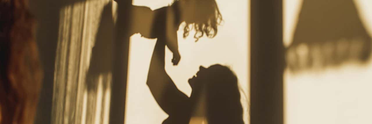 Silhouette of mom parent lifting baby.