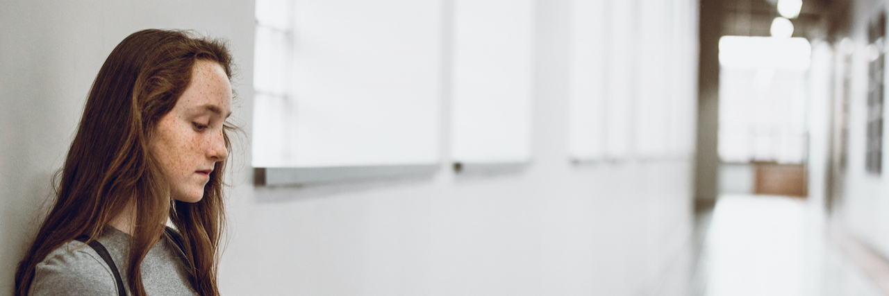 Eating Disorder Triggered by Traumatic Divorce Teen girl leaning against wall at school holding notebook