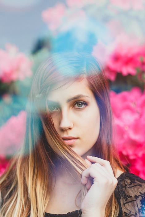 Ashley holding hair in front of her face in front of flowers.