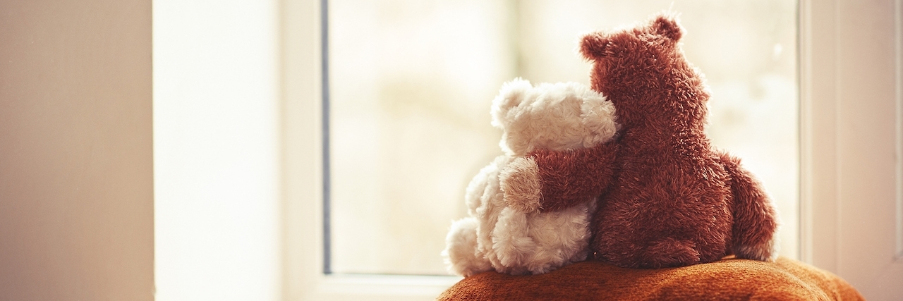 Losing Friends Because of Chronic Pain Two embracing teddy bears looking through the window sitting on window-sill.
