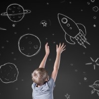 Little boy reaching for rocket in drawn space