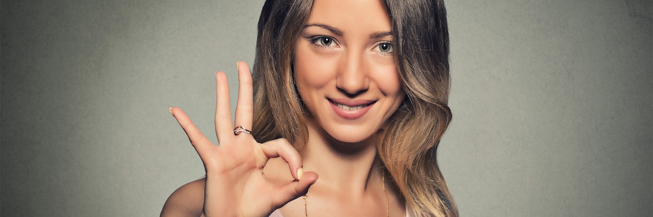 Chronic Pain: How I Respond When Someone Asks How I'm Feeling Beautiful happy young woman showing Ok sign isolated on gray wall background.