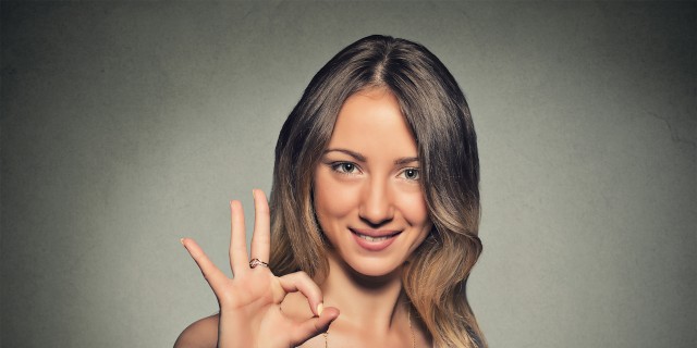 Beautiful happy young woman showing Ok sign isolated on gray wall background.