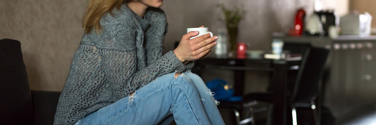 Sad Woman sitting at Home holding Coffee Mug