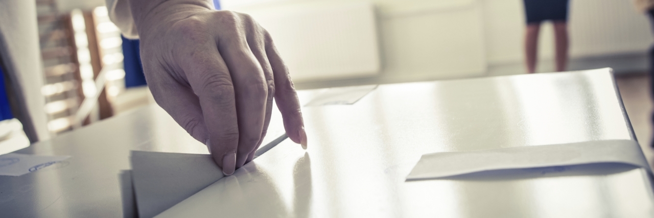 A hand deposits a ballot into a voting box.