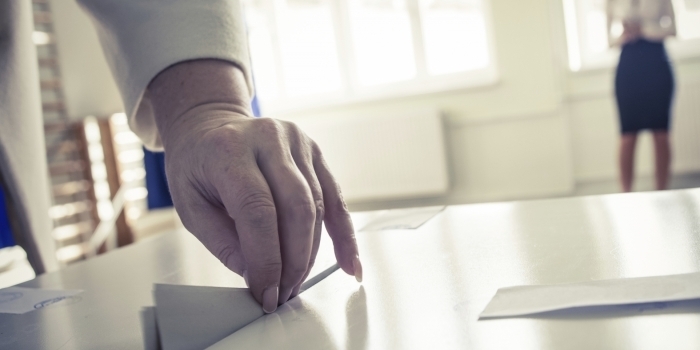 A hand deposits a ballot into a voting box.