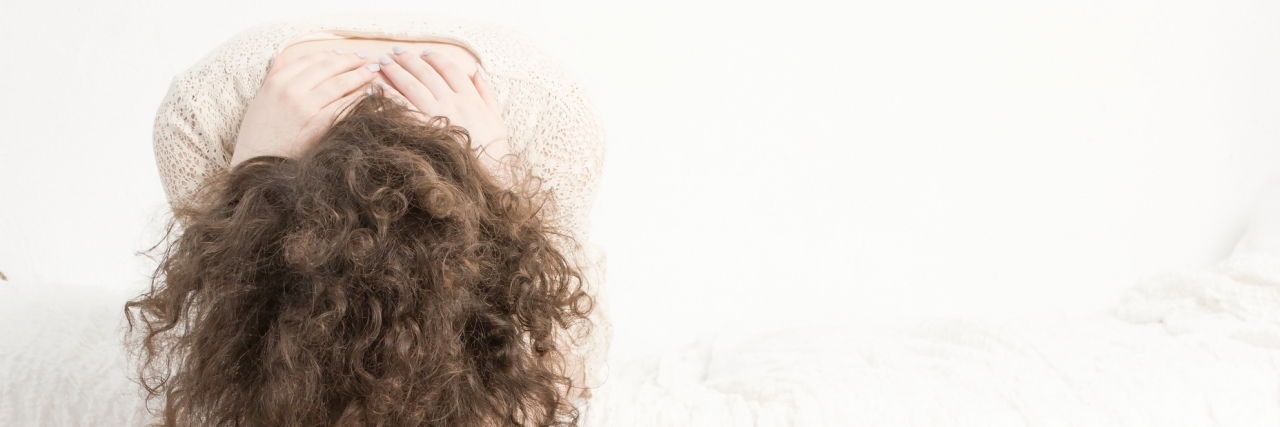 A Letter to Myself When I'm Manic woman sitting on bed with head between her knees, overwhelmed by racing thoughts