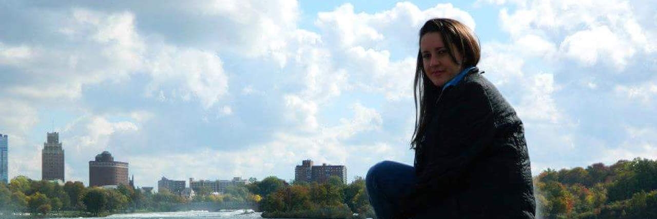 Judgment and Unrealistic Expectations About My Fibromyalgia woman sitting on a rock with a river and skyline int he background