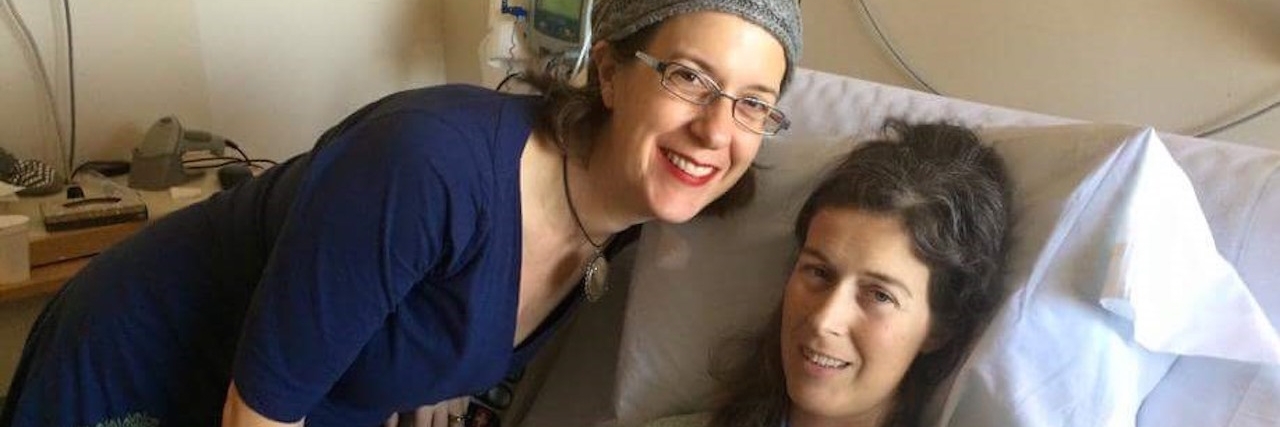 How to Answer 'What Do You Do?' as a Woman With Rheumatoid Arthritis woman lying in hospital bed with her sister standing next to her