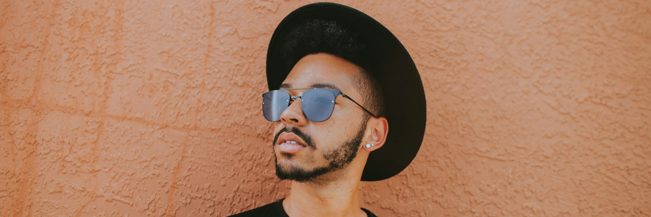Tips for Lupus Symptoms in the Summer Black man wearing hat and sunglasses, leaning against a bright wall