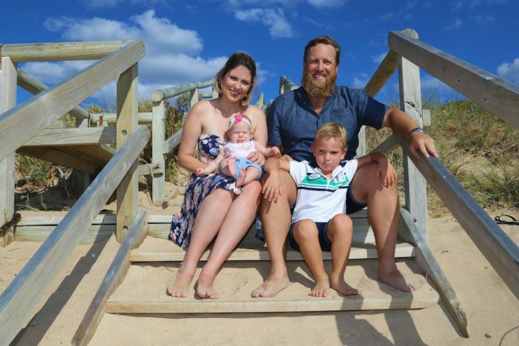 a family including mom dad baby girl and young son sitting on a staircase outdoors by a beach