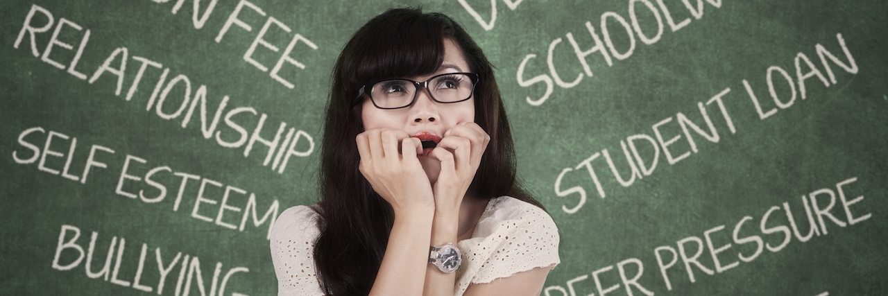 student sitting in front of a table of books with words written on a chalk board behind her showing her stressors