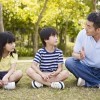 Father talks to daughter and son as tehy sit outside on grass