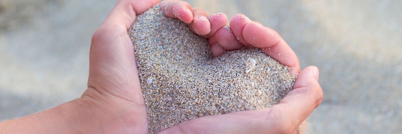 Woman holding handful of sand shaped like a heart