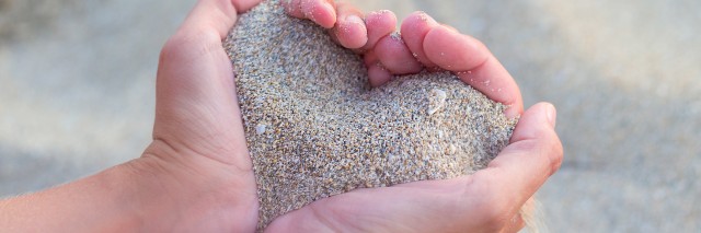 Woman holding handful of sand shaped like a heart